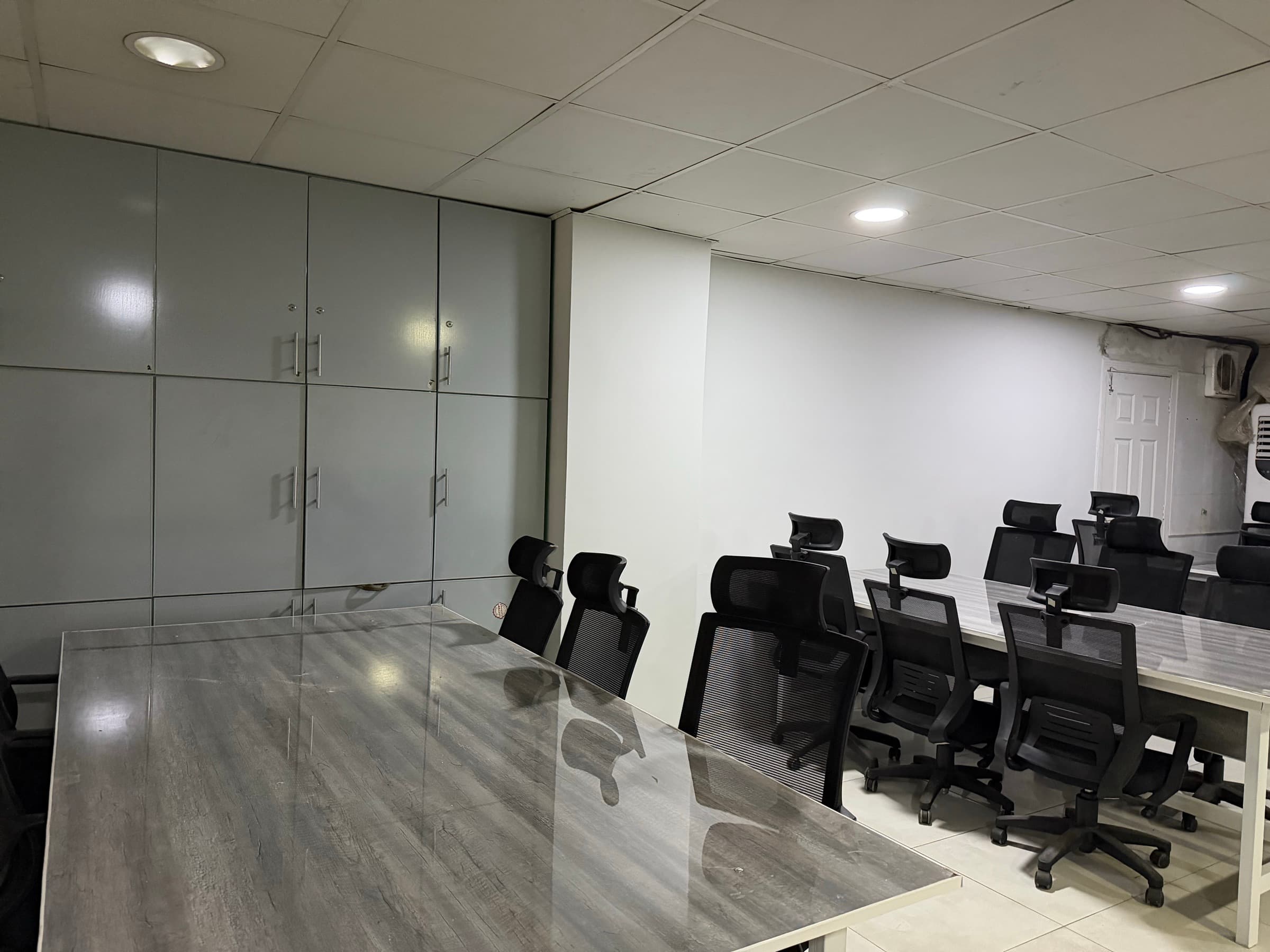 A room on the floor with full-height storage cupboards along one wall and a row of desks and chairs beside it.
